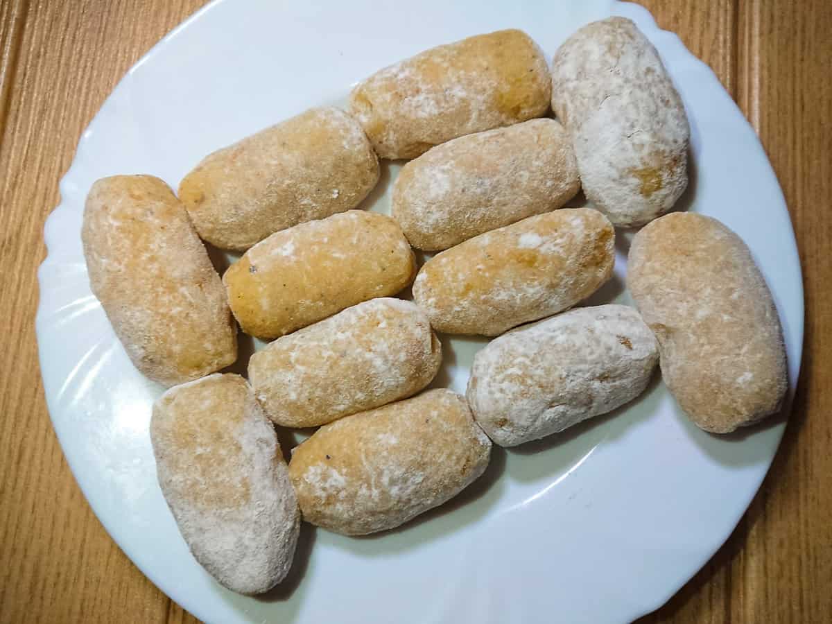 Uncooked potato croquettes with cheese rolled in flour on a white plate.