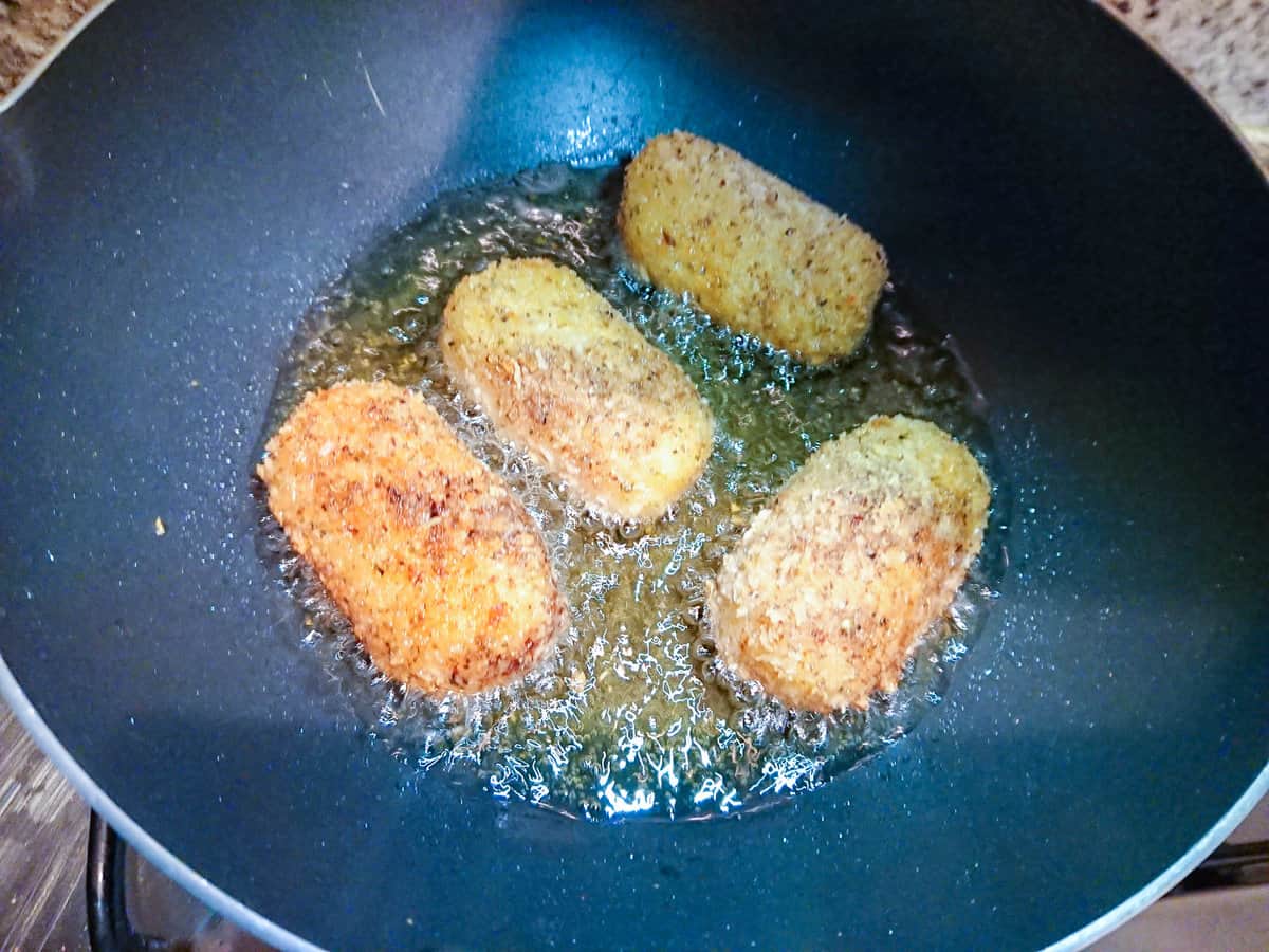 Potato croquettes with cheese being fried in oil in a deep pan.