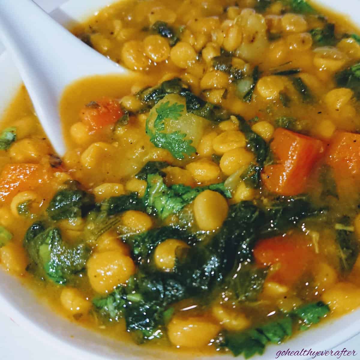 close up view of chana dal soup in a white ceramic bowl with a spoon in it.