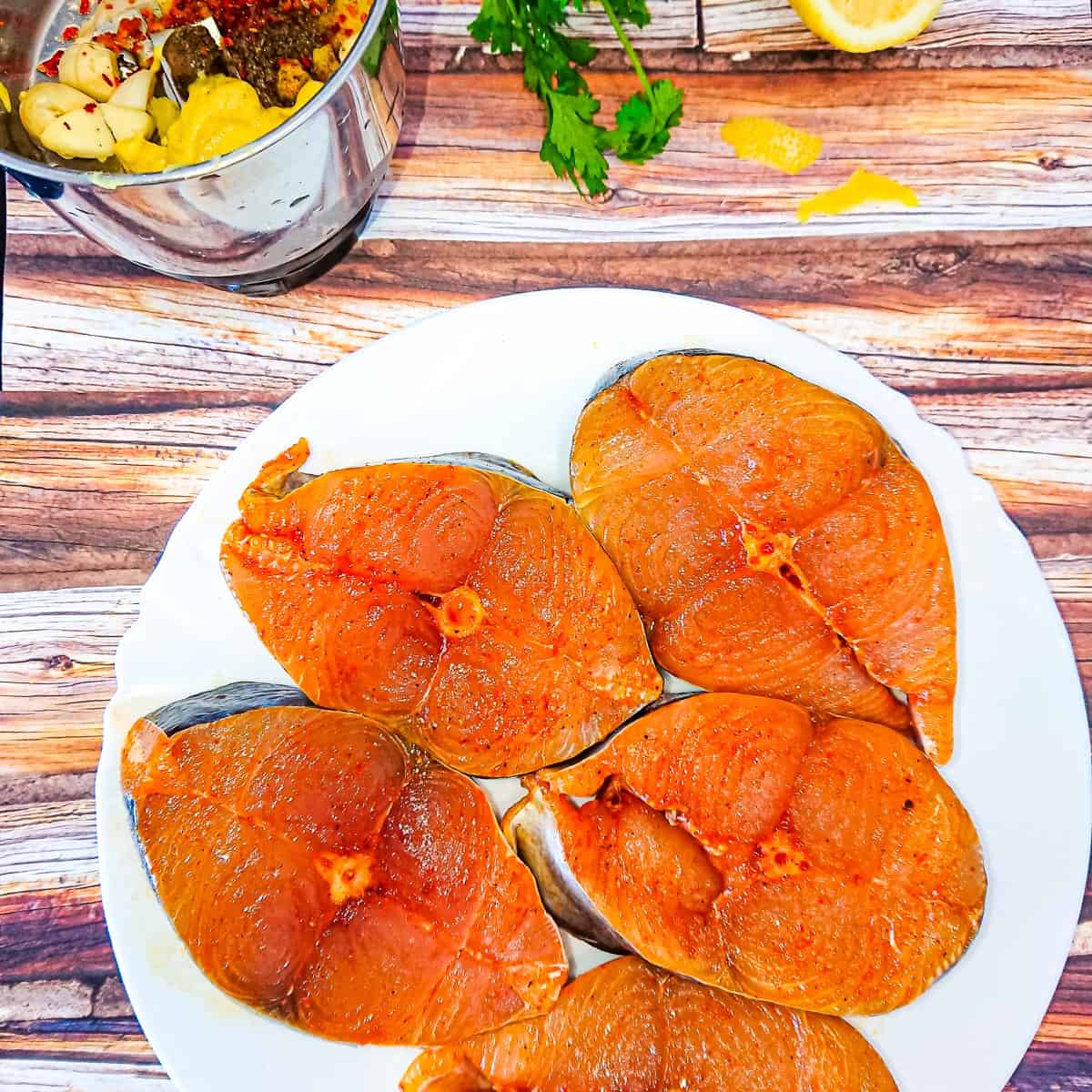 Mackerel fish steaks seasoned with chilli powder and salt on a white plate.