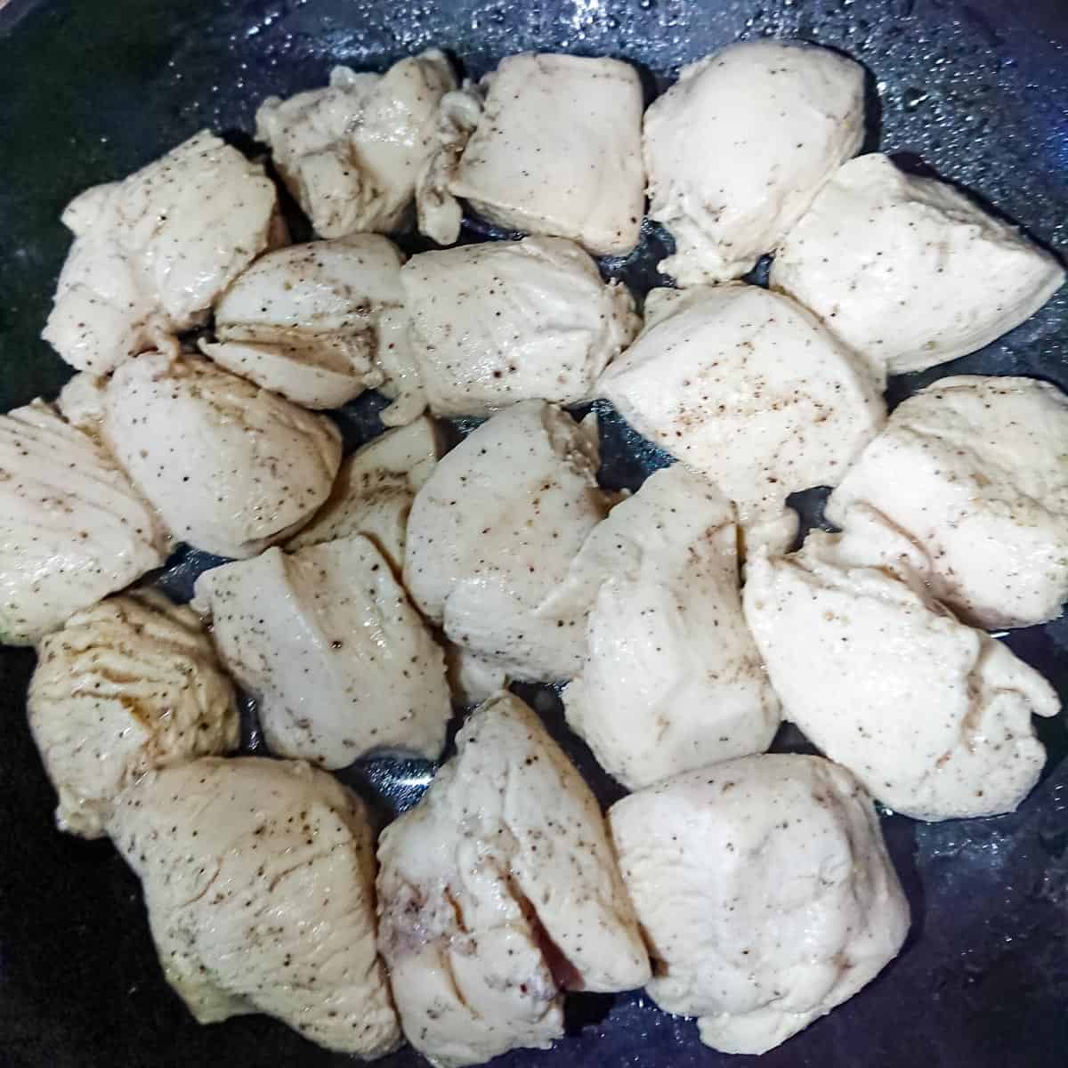 chicken being sauteed in a non stick pan for yogurt lemon chicken.