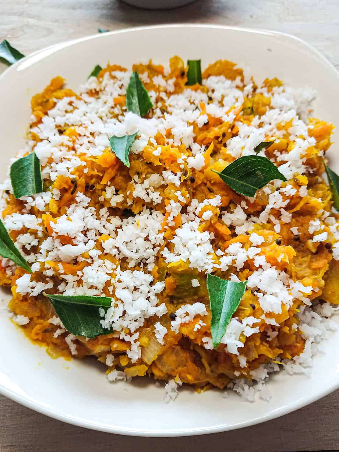 recipe for mashed pumpkin garnished with coconut and curry leaves in a white plate.