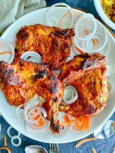 tandoori roast chicken legs on a white plate and a bowl full of biriyani on the upper right corner.