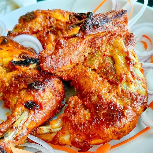 closeup view of roast tandoori chicken quarters. legs on a white plate.