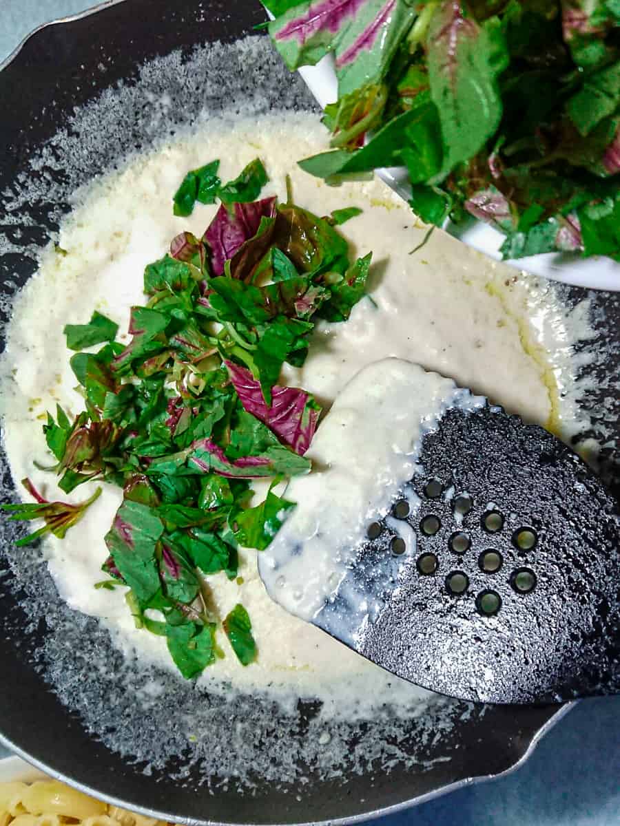 Chopped spinach being added to vegan garlic sauce for pasta.