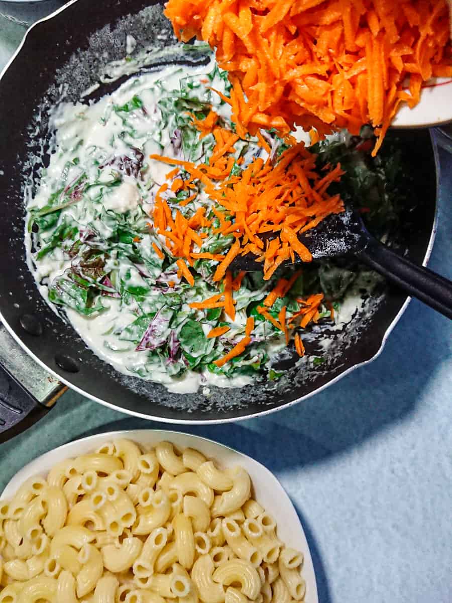 Grated carrots being aded to vegan garlic sauce with spinach.