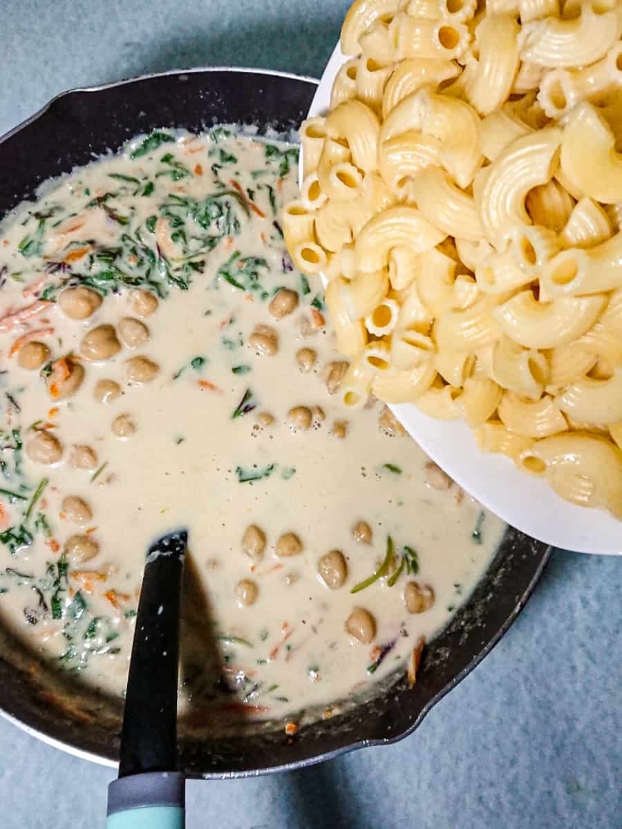 Adding pasta to the creamy garlic sauce.