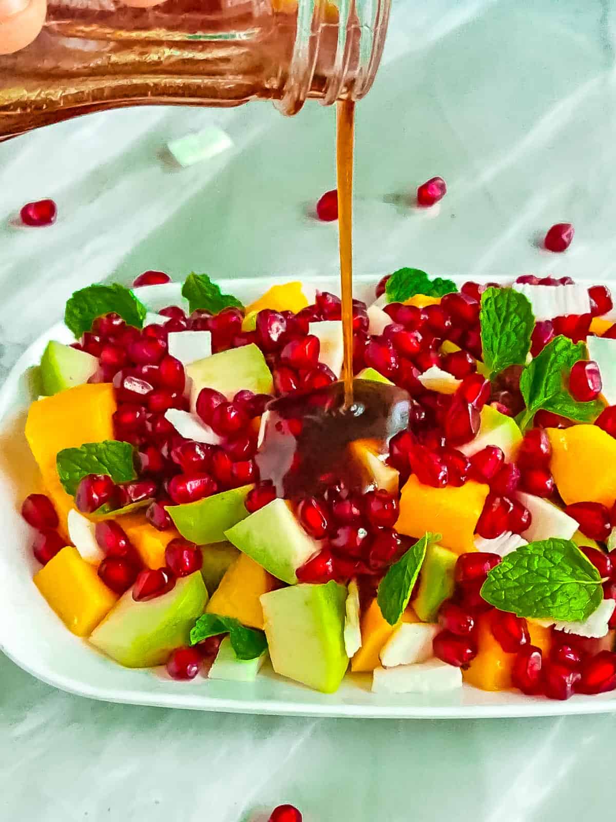 Indian salad dressing being drizzled on mixed fruit chaat.