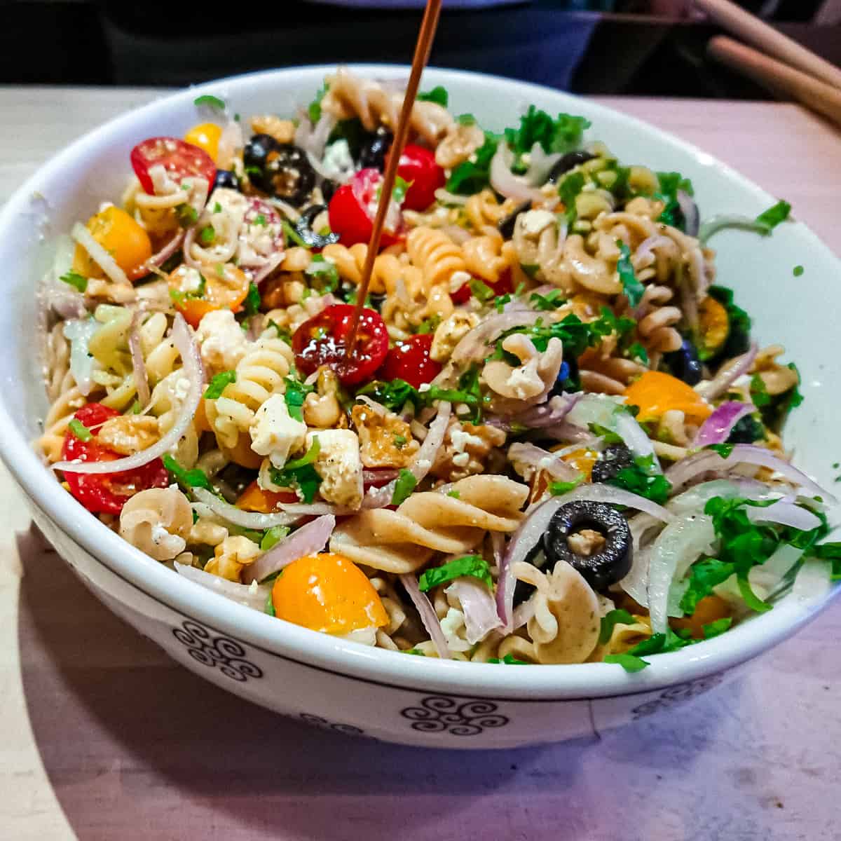 easy balsamic pasta salad in a white ceramic bowl with basil balsamic vinaigrette being drizzled on it.