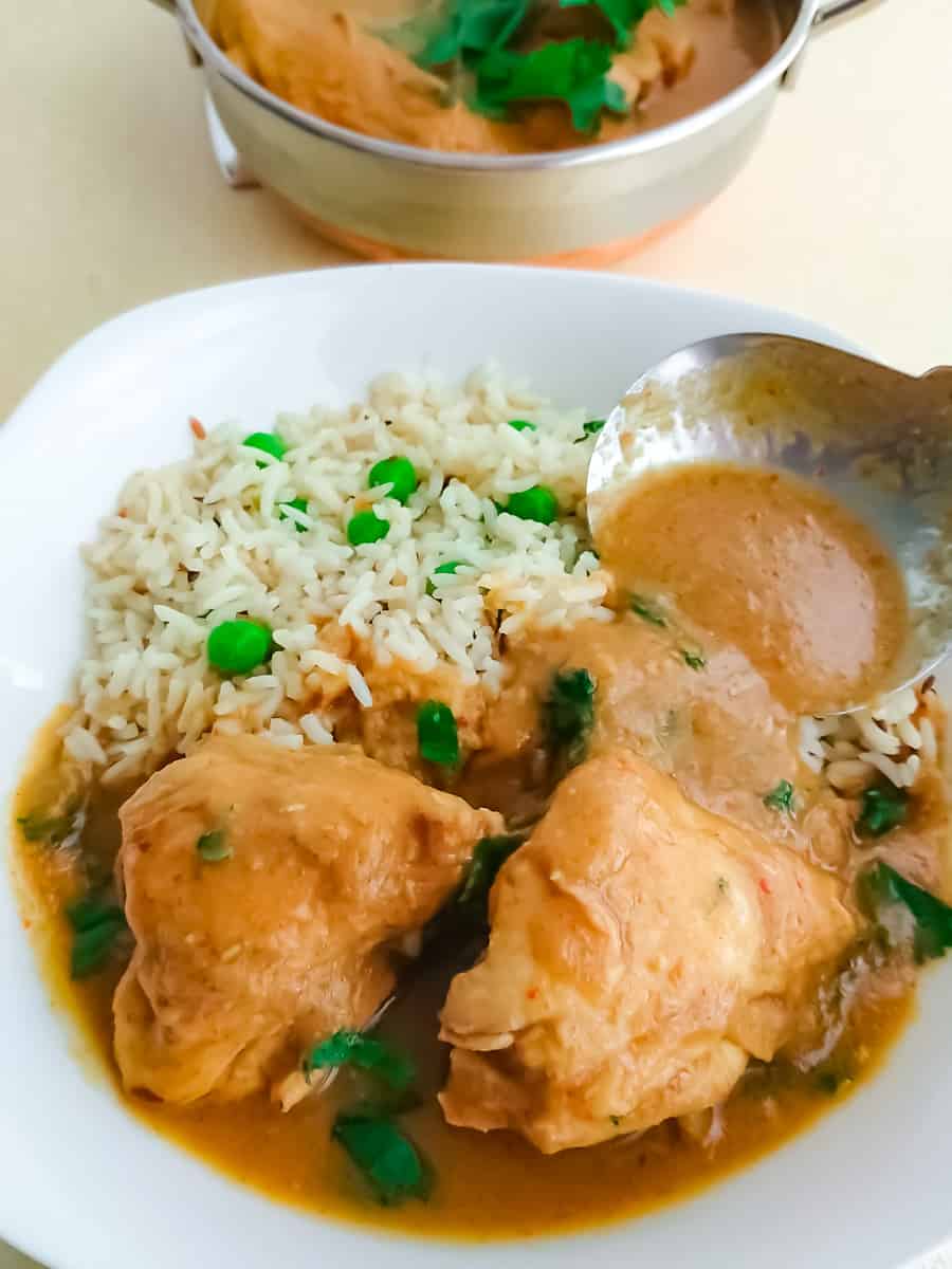 chicken curry without coconut milk served with peas pulao and a stainless steel bowl full of curry in the background.