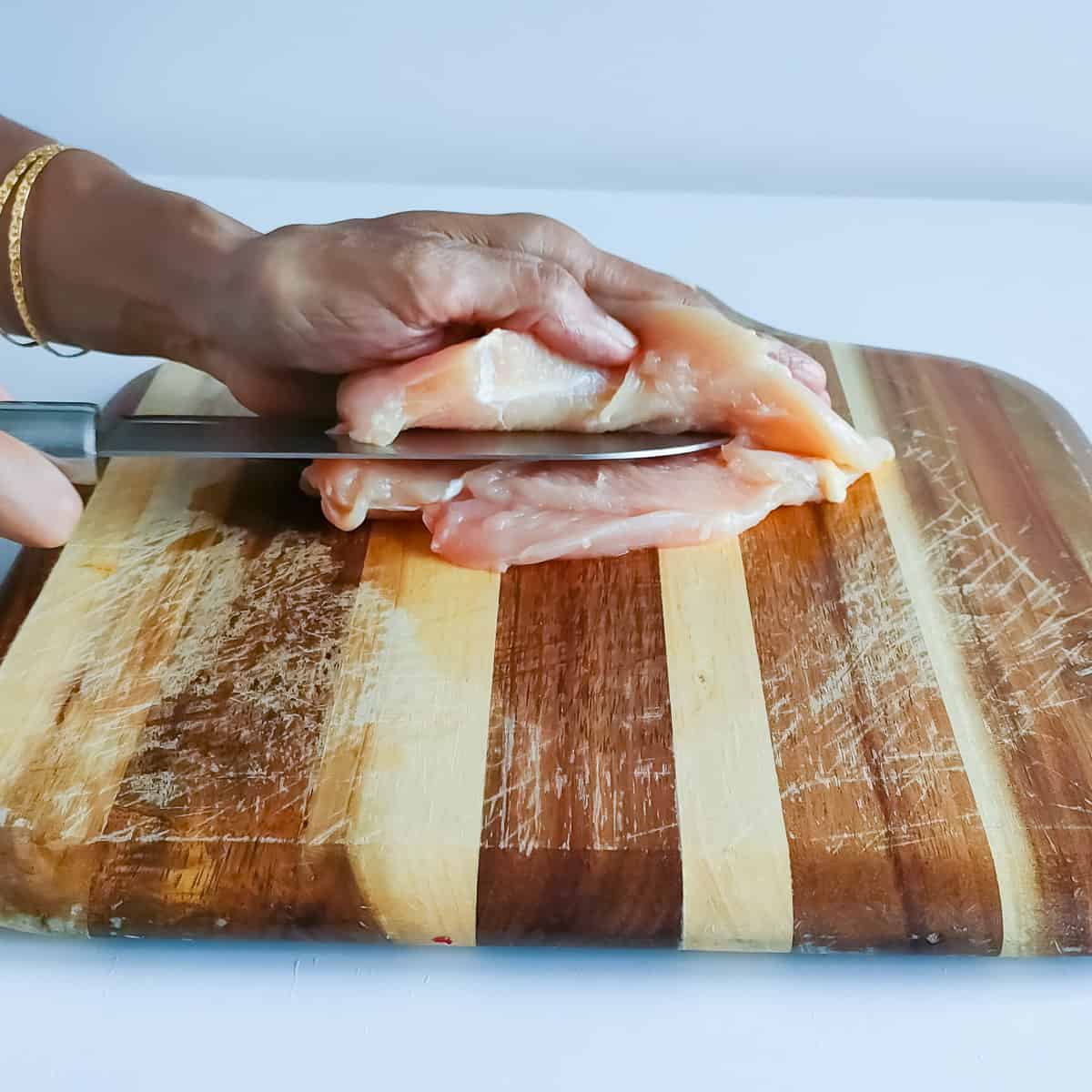 Chicken breast being thinly sliced with a knife on a chopping board.