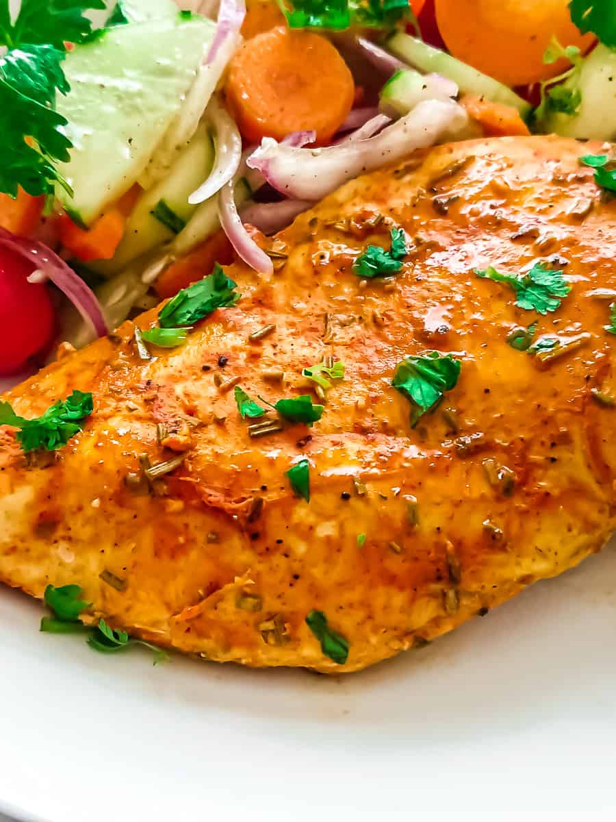 closeup view of easy baked thin sliced chicken breast served with garden salad in a white ceramic plate