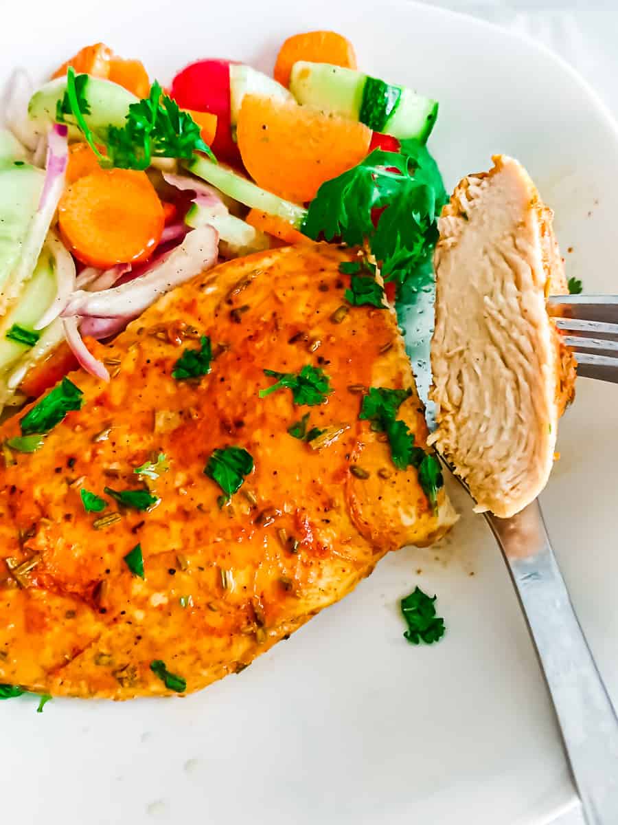 closeup view of oven baked thin sliced chicken breast boneless served with garden salad in a white ceramic plate