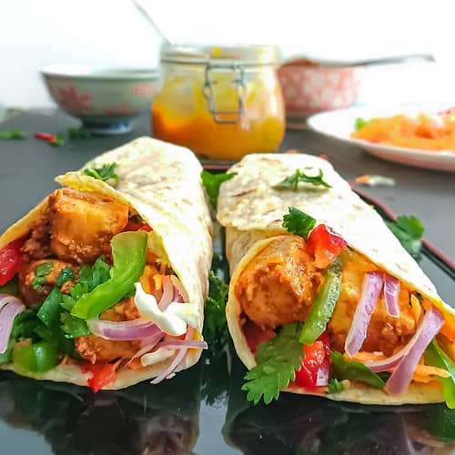 paneer kathi rolls on a black plate with mango chutney and veggies