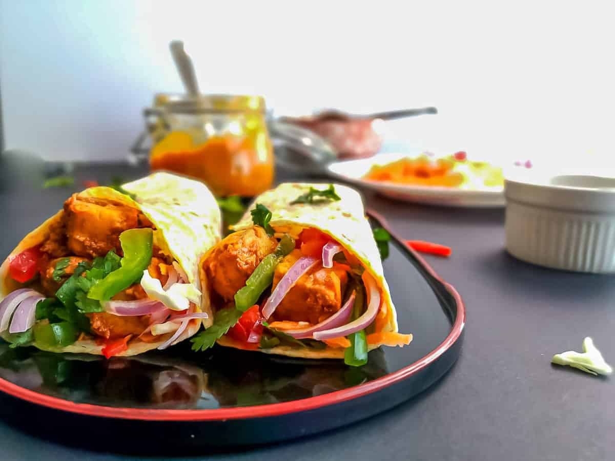 paneer kathi rolls on a black plate with mango chutney and veggies.