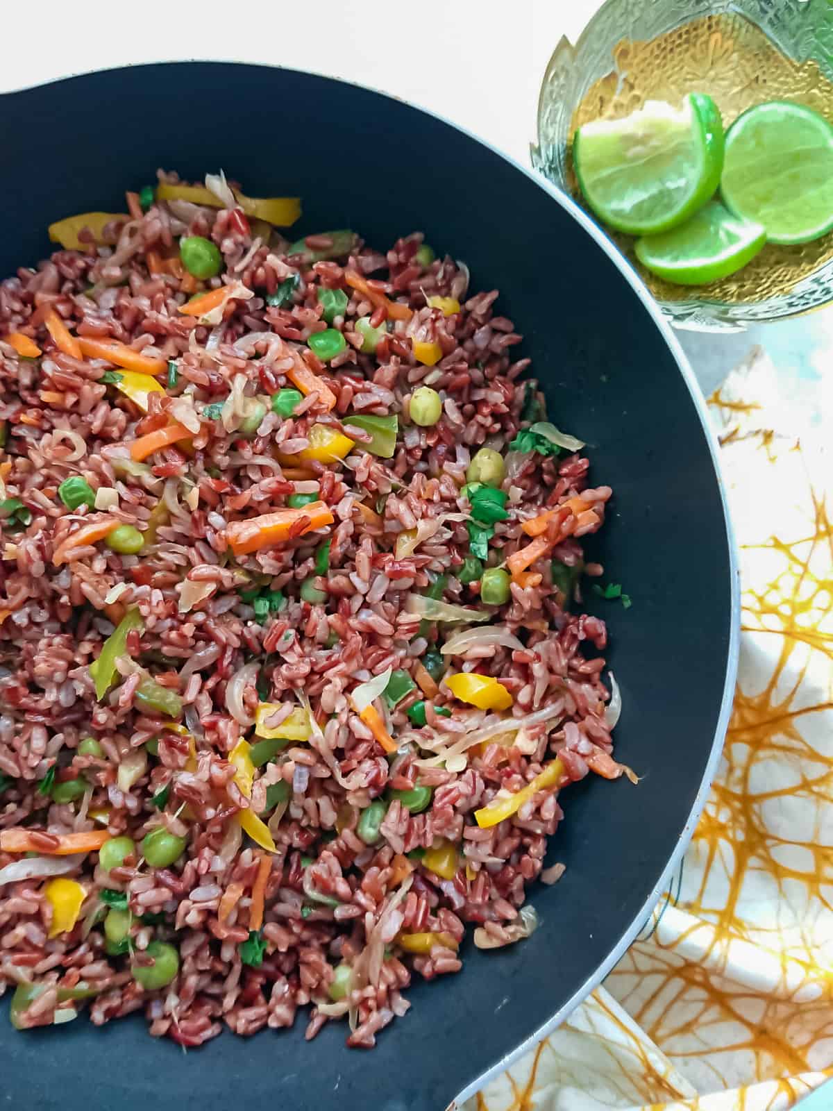 close up view of red fried rice in a pan with lime wedges