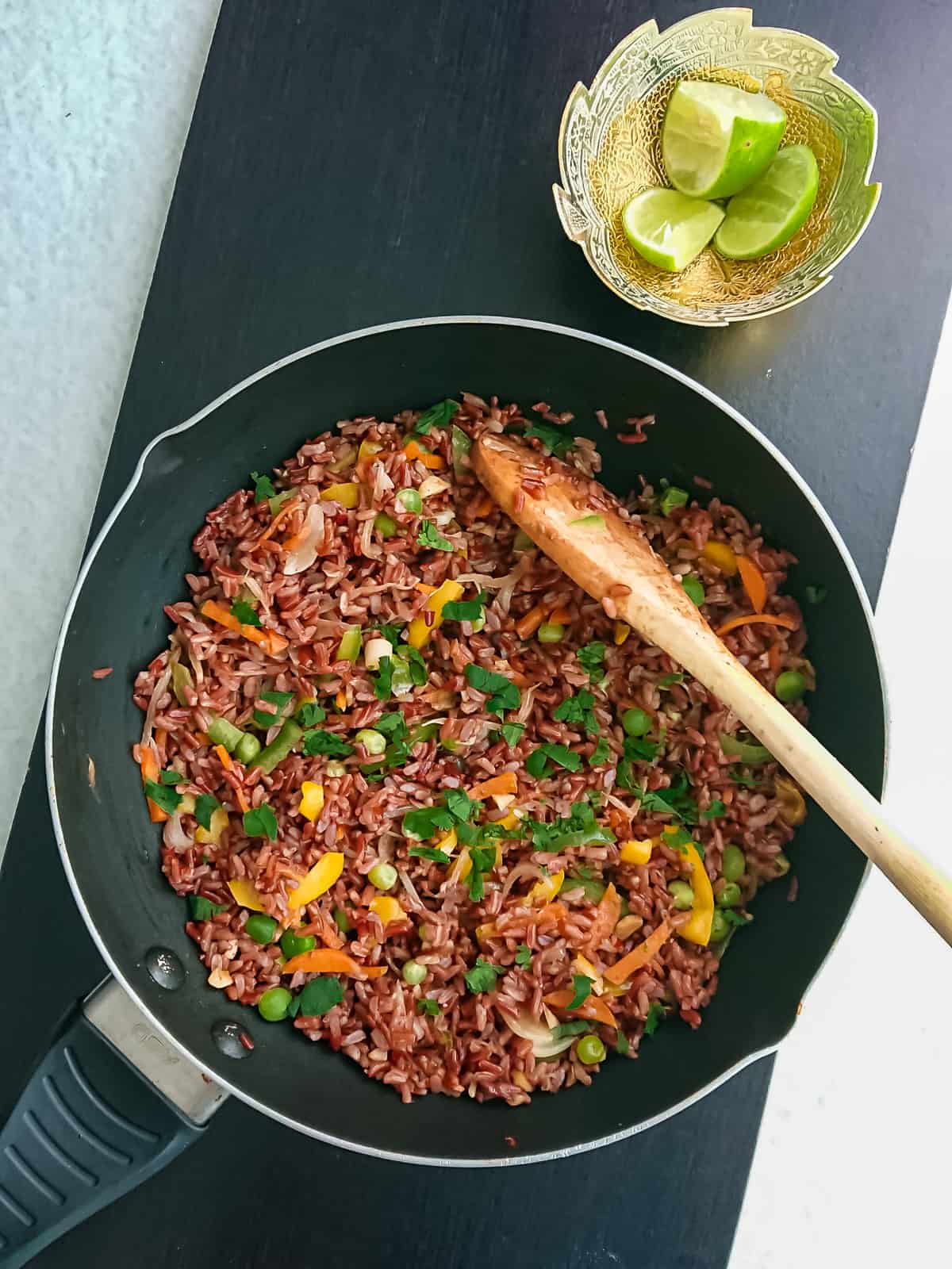 Healthy fried rice with red rice in a wok pan  with lime wedges in a bowl next to it.