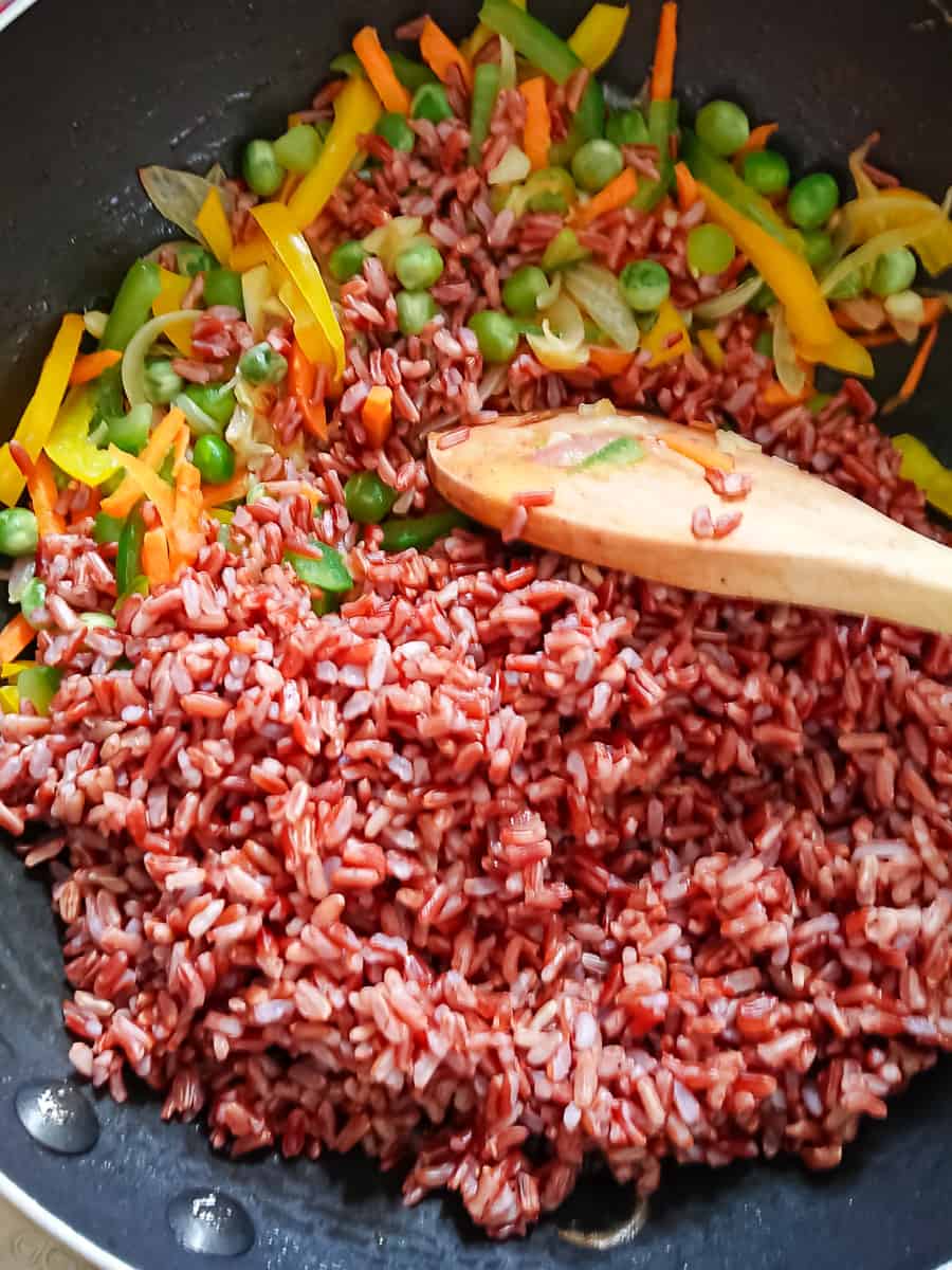 red rice being stir-fried with vegetables in a wok.