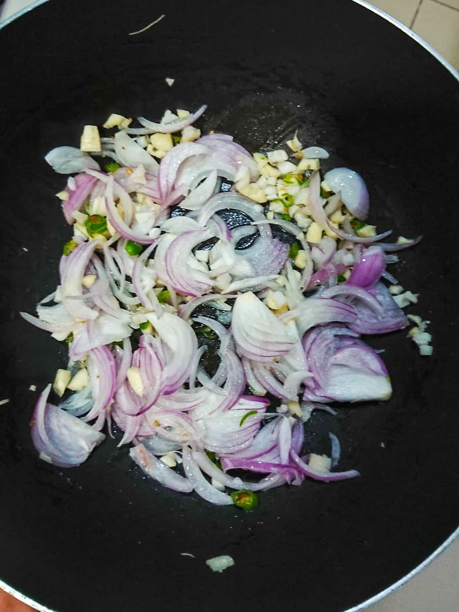 onions, garlic and chili being stir-fried in oil in a wok pan.