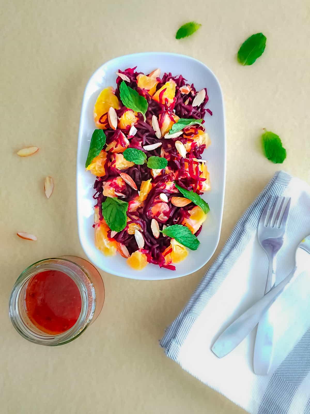 Beet and Mandarin Orange Salad with Mint in a white plate and a jar of citrus ginger dressing.