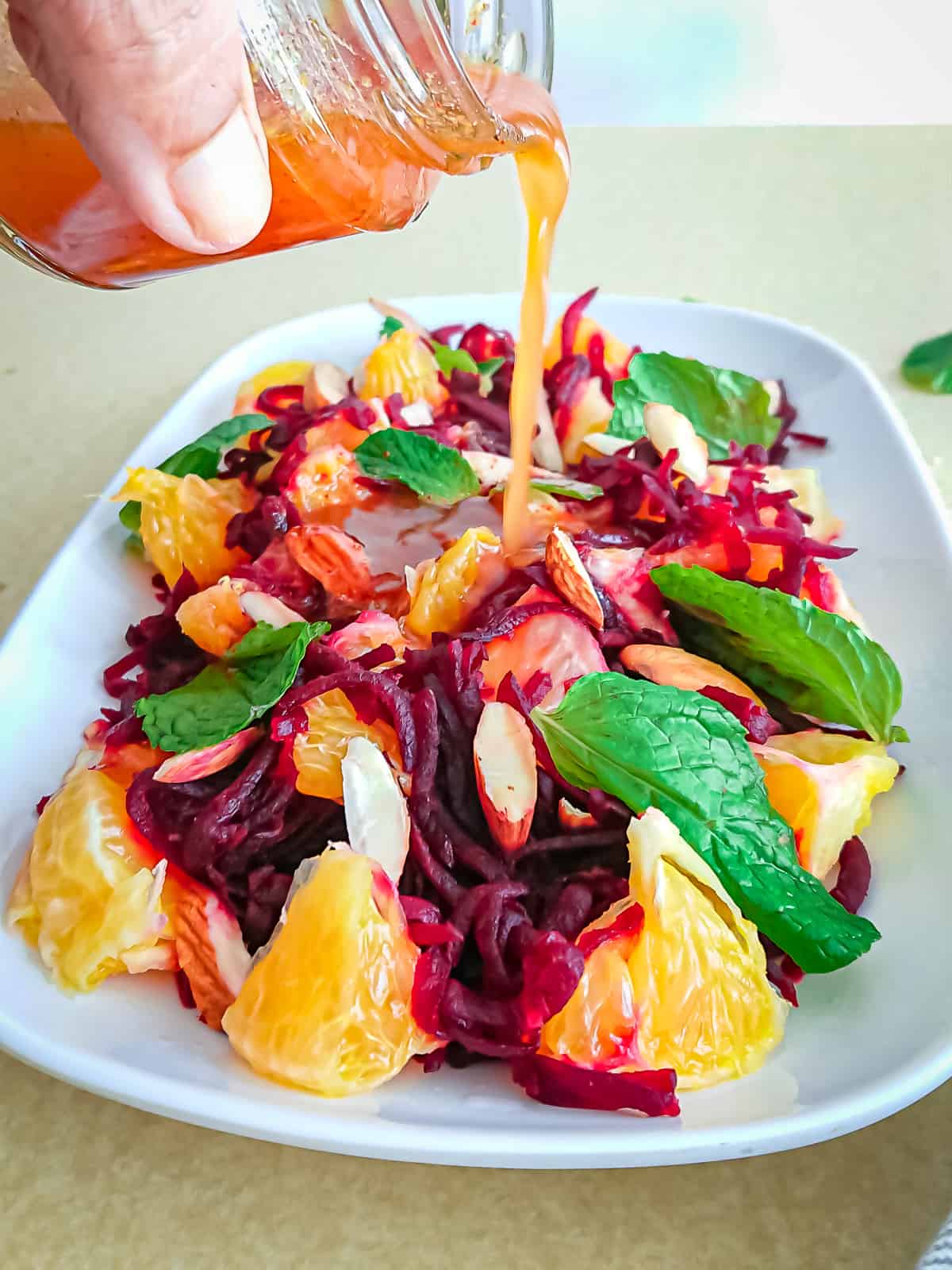 closeup view of ginger lemon dressing being poured on beet and mandarin orange salad on a white plate.