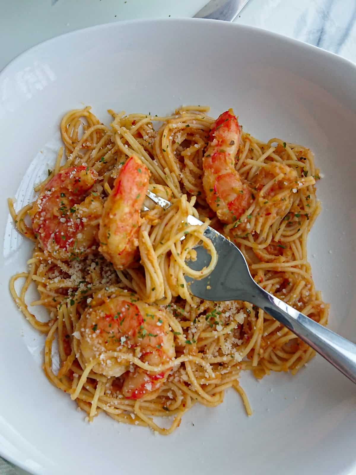 closeup view of tomato prawns with pasta in a white plate with a fork.