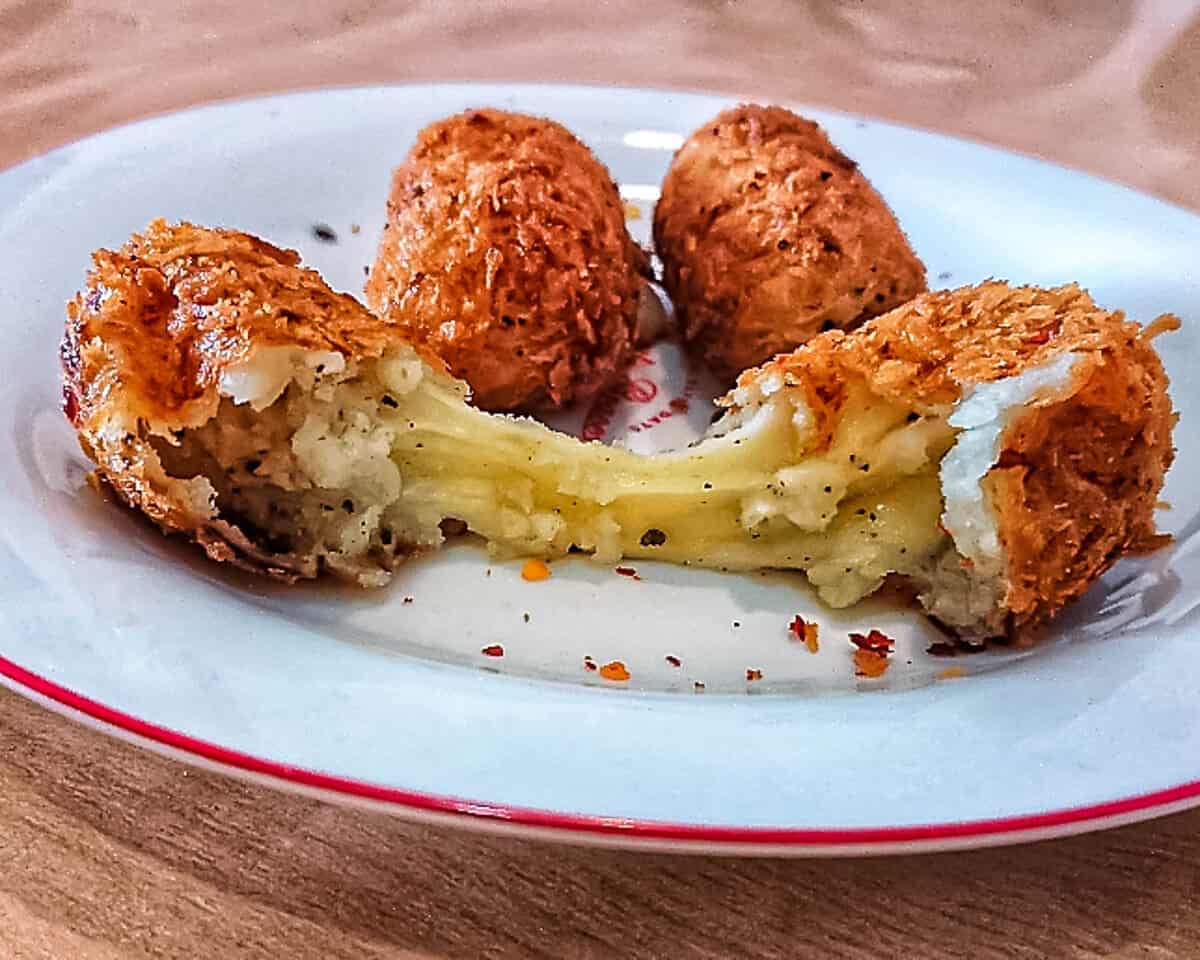 closeup view of Italian croquettes with cheese oozing out on a white ceramic plate.