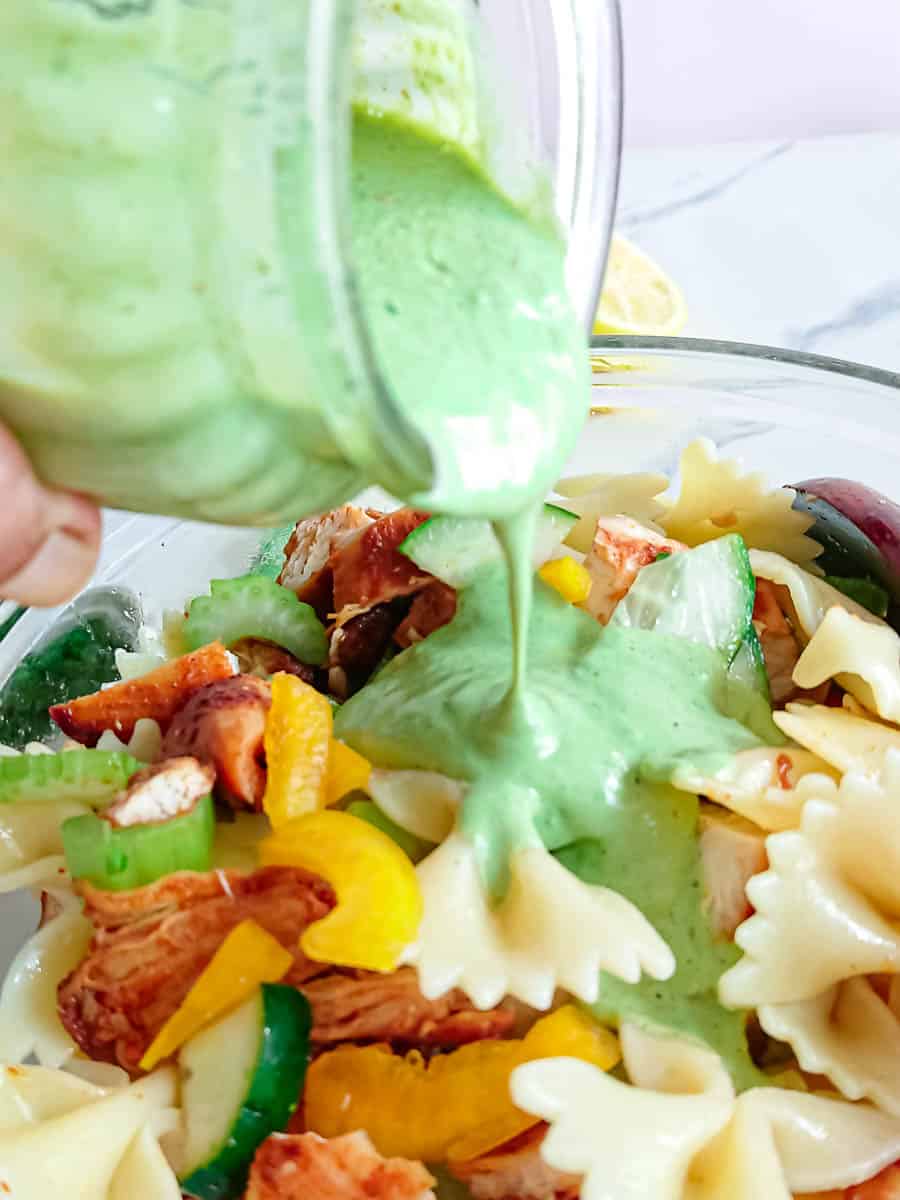 Close up view of Greek yogurt dressing being poured on high protein pasta salad in a glass bowl.