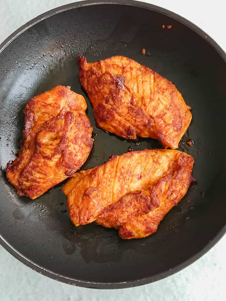 thinly sliced marinated chicken breasts being pan-seared in a non-stick pan.