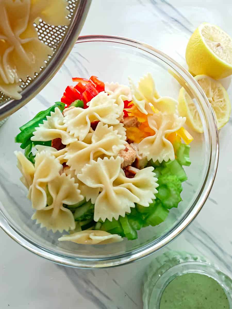 Pasta being added to vegetables and chicken in a glass bowl.