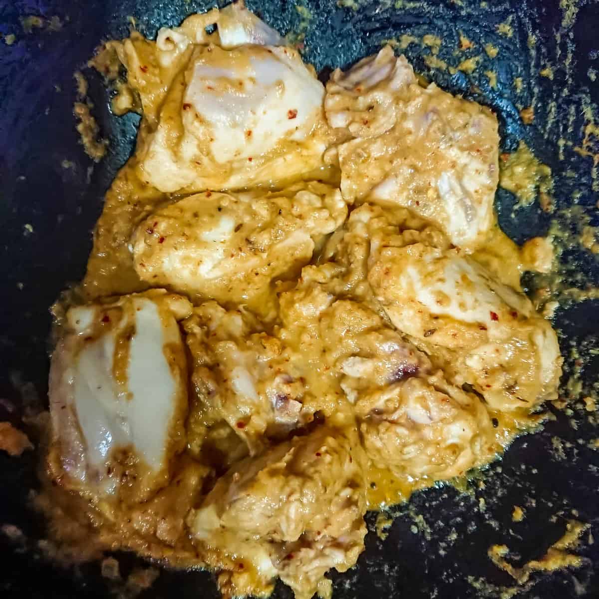 Chicken thighs being sauteed with curry paste in a pan, for easy Indian chicken curry.