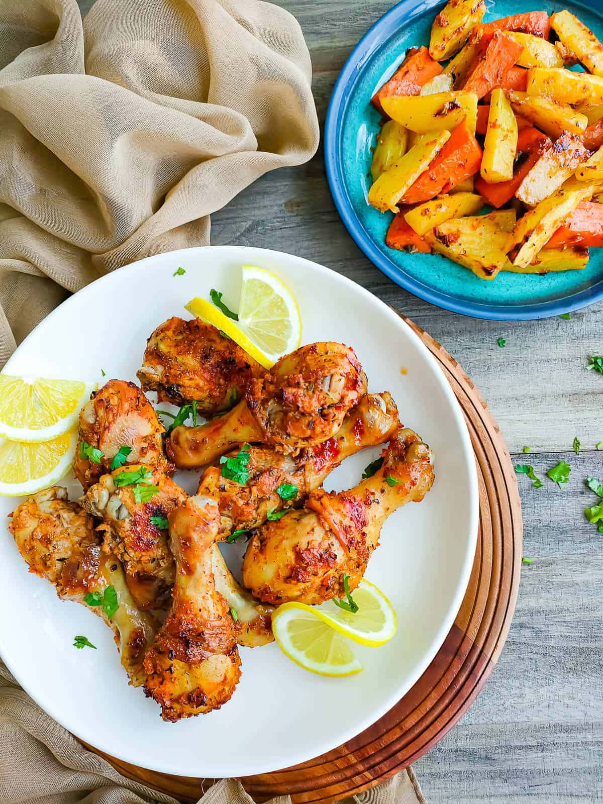 sheet pan chicken legs in a white plate & roasted potatoes & sweet potatoes in a blue bowl.