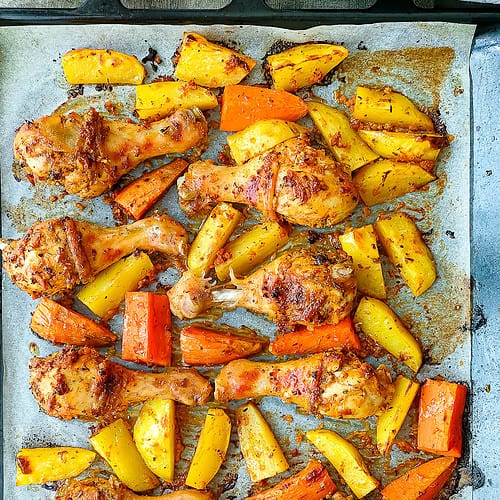 one pan roasted chicken legs and potatoes and sweet potatoes on a baking sheet.