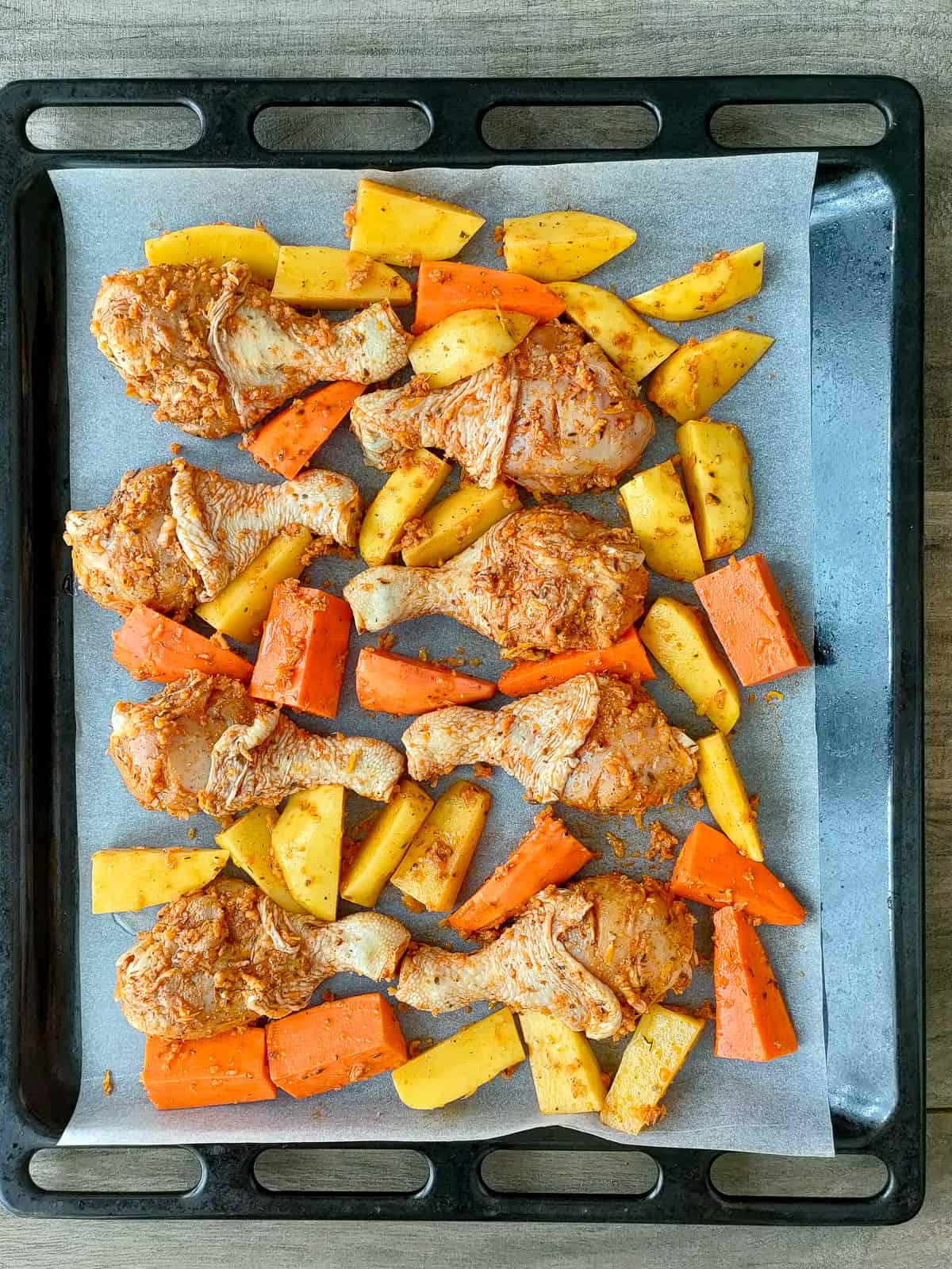 chicken drumsticks and potatoes and sweet potatoes with herb and garlic seasoning on a baking sheet.