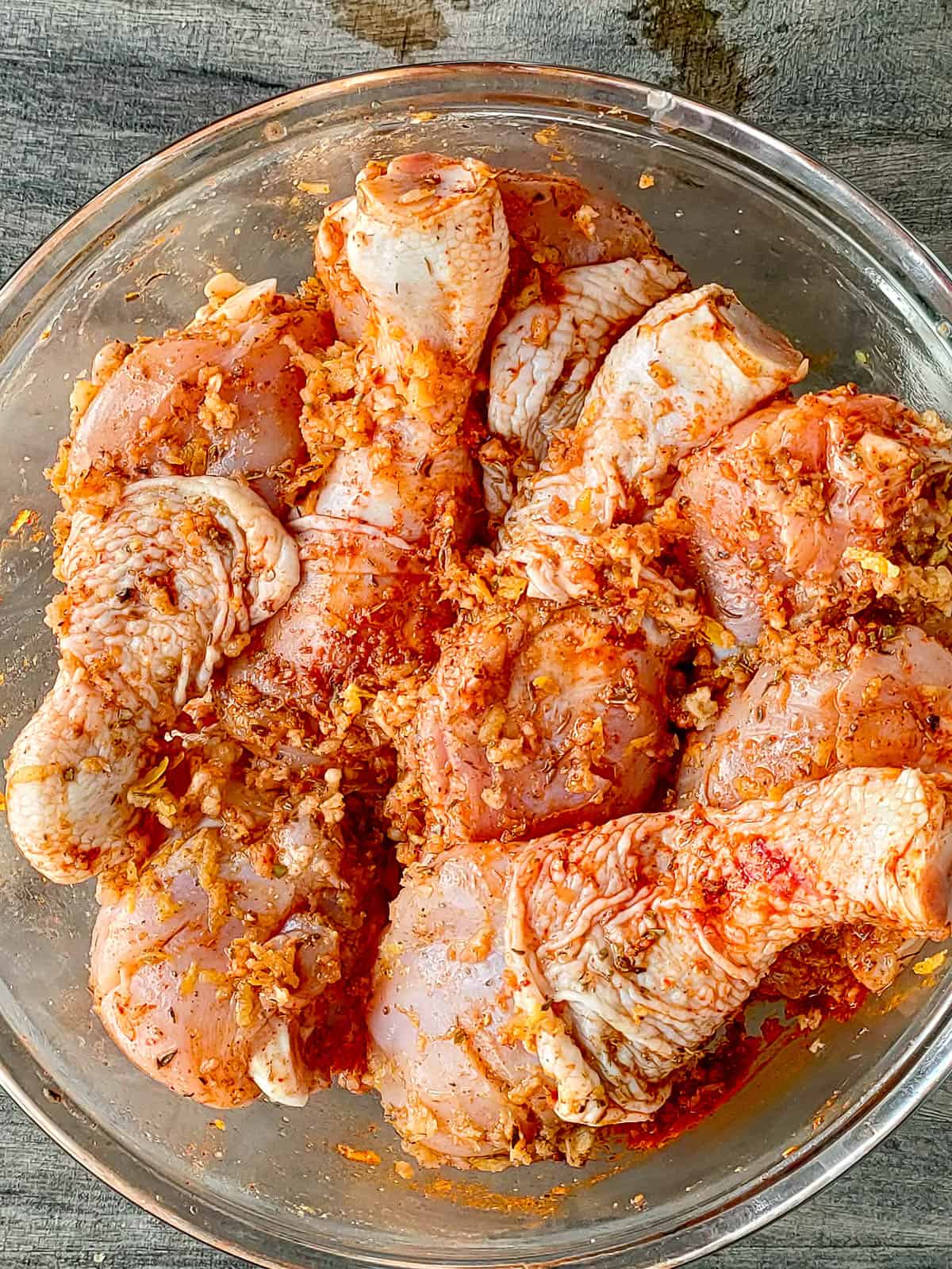 Chicken drumsticks marinated with garlic and herb seasoning in a glass bowl.