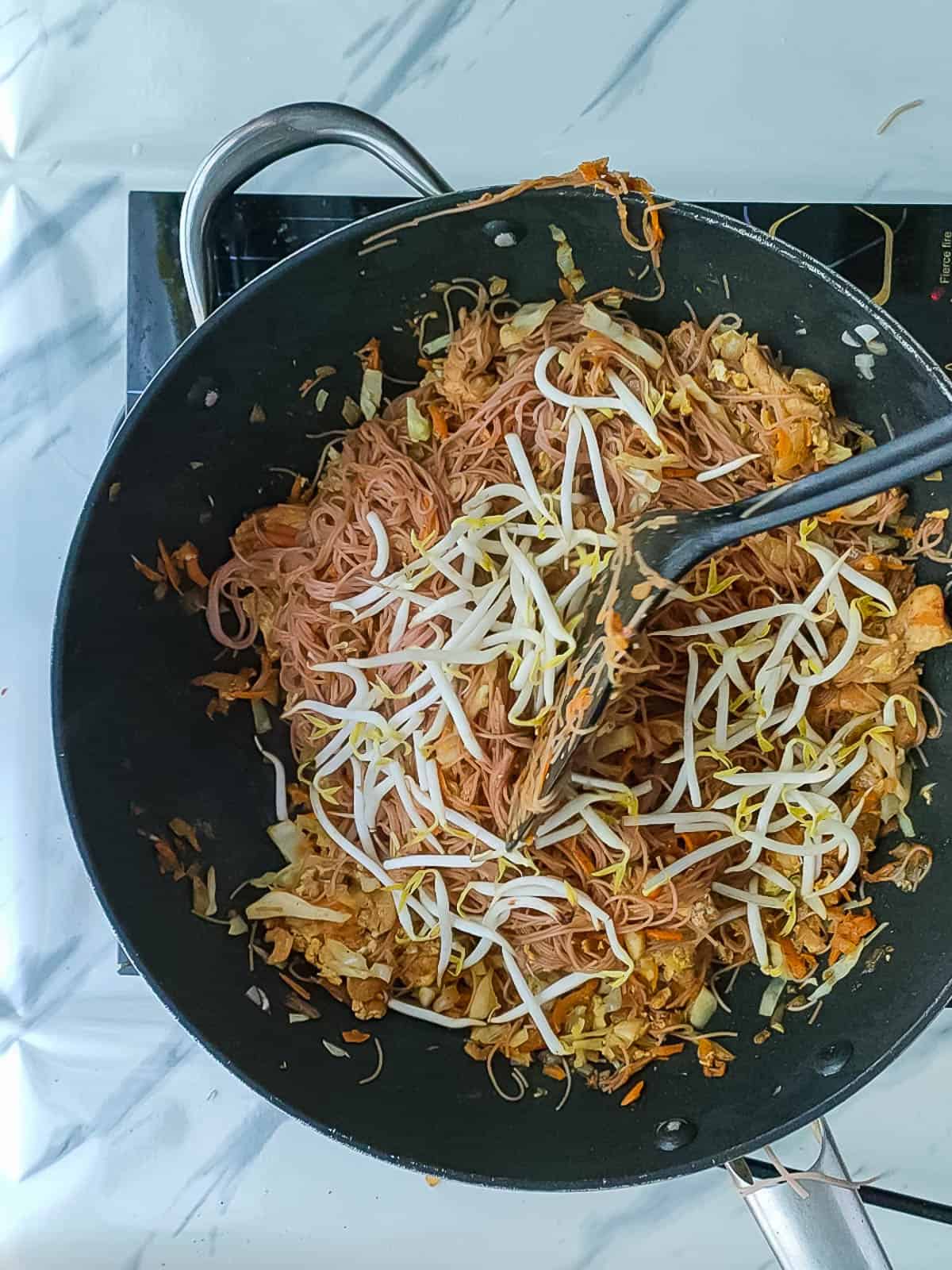 Singapore fried bee hoon being stir-fried with bean sprouts in a non-stick wok.