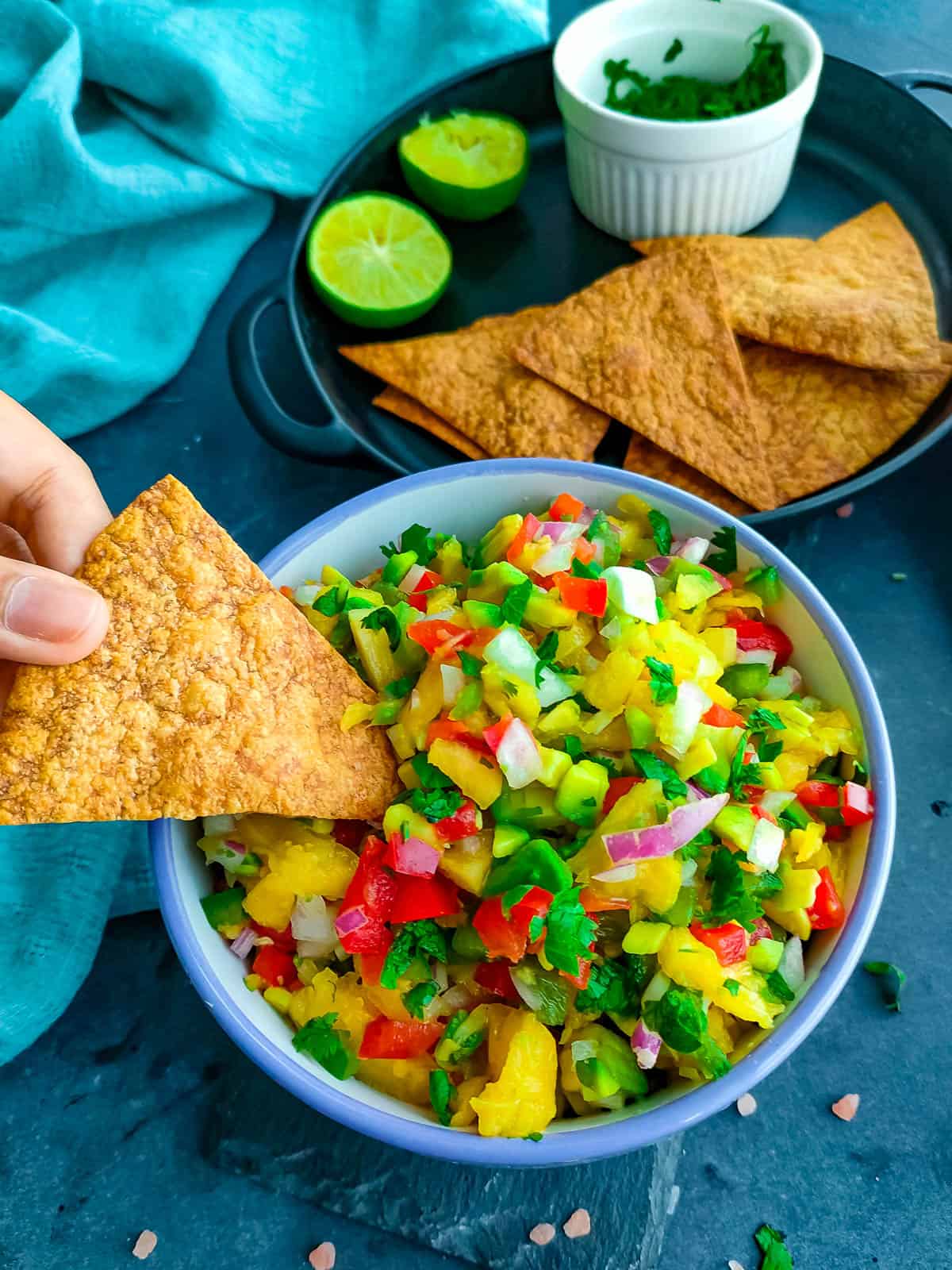 Pineapple Pico de Gallo Salsa with Avocado pineapple jalapeno salsa in a white bowl and wholewheat tortilla chips in a black plate and cilantro in a small bowl.