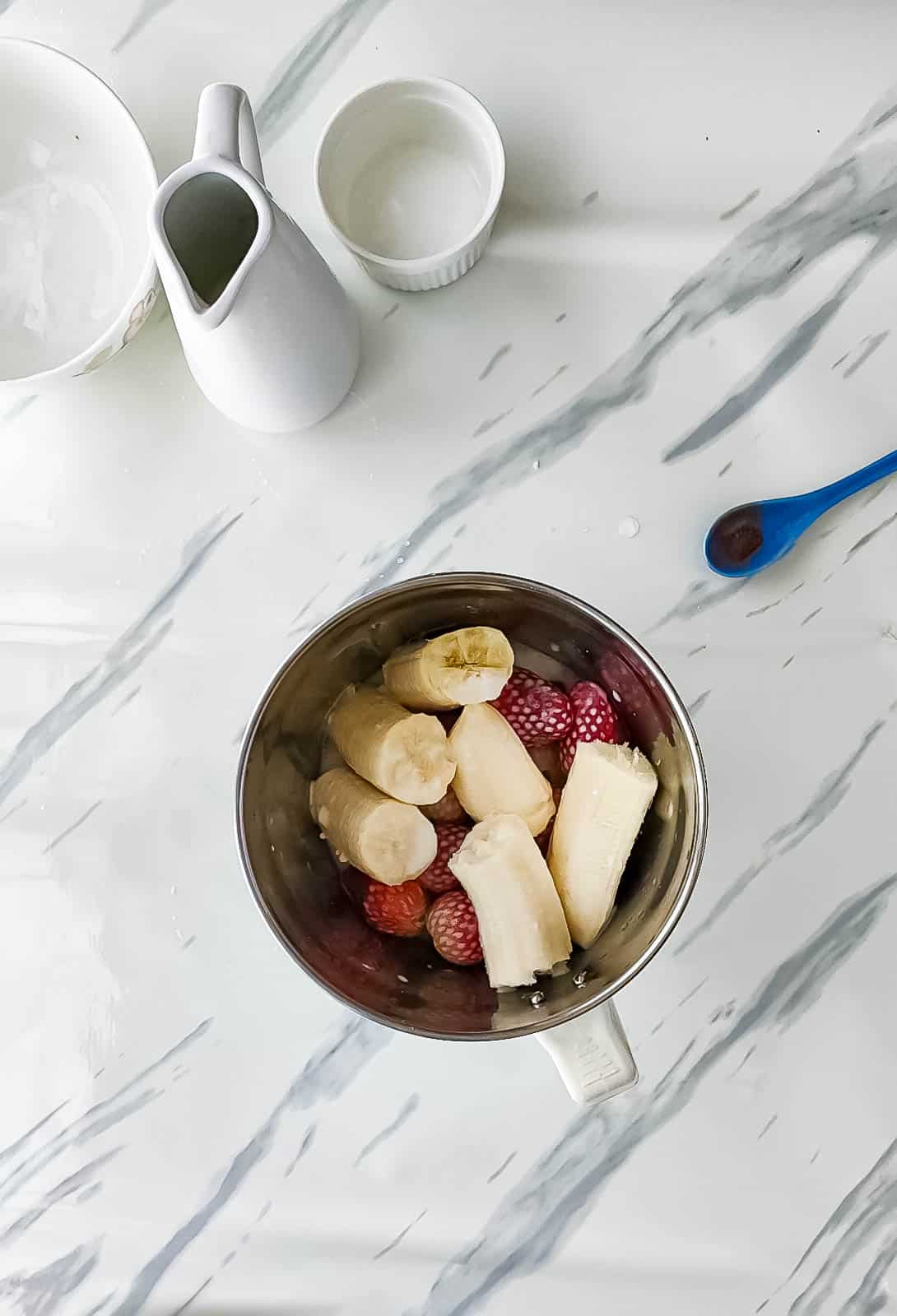 Ingredients for no-ice cream strawberry banana milkshake in a blender jar.