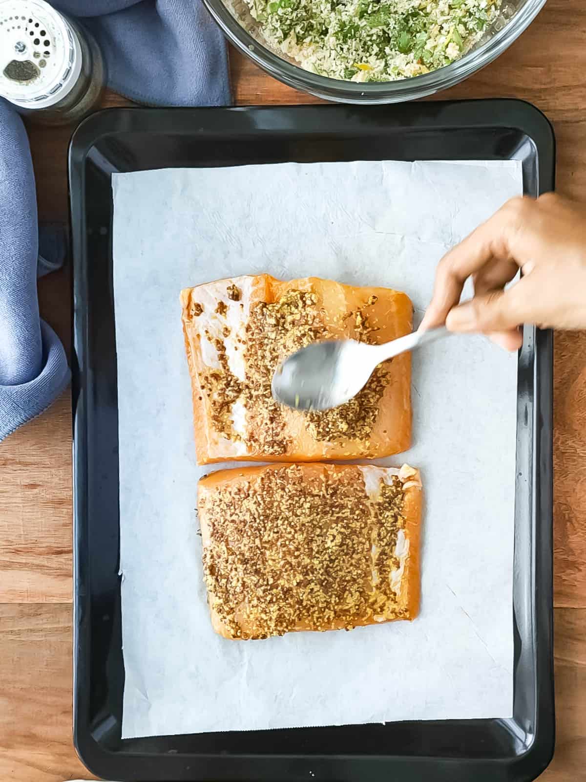 2 fish fillets being coated with wholegrain mustard.