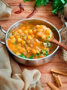 Authentic chana masala in a metal bowl with curry scooped out in a ladle.