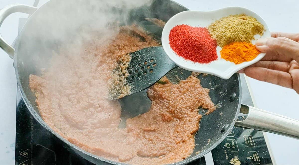 Spices being added to onion tomato paste for chana masala gravy.