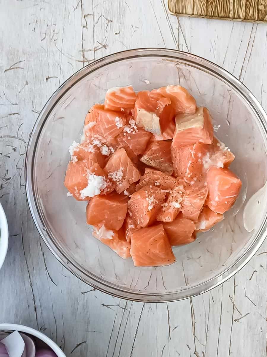 Salmon cubes seasoned with salt and pepper in a glass bowl.