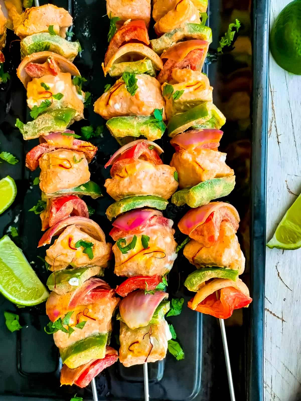 Baked salmon kabobs in oven with onions and peppers on a black tray.