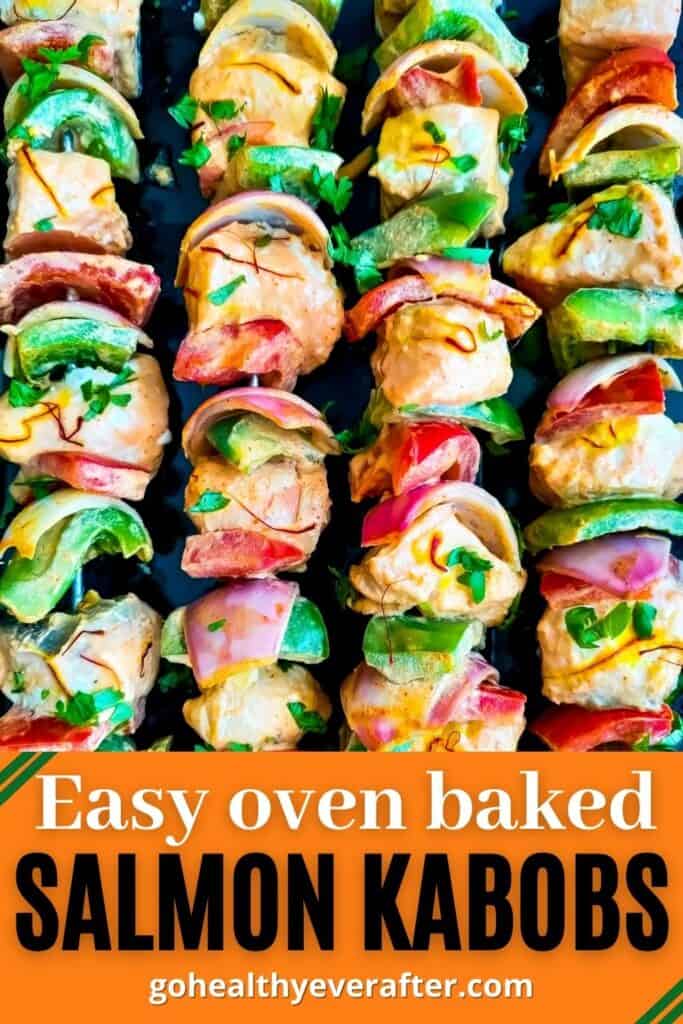 Baked salmon kabobs in oven with onions and peppers on a black tray.