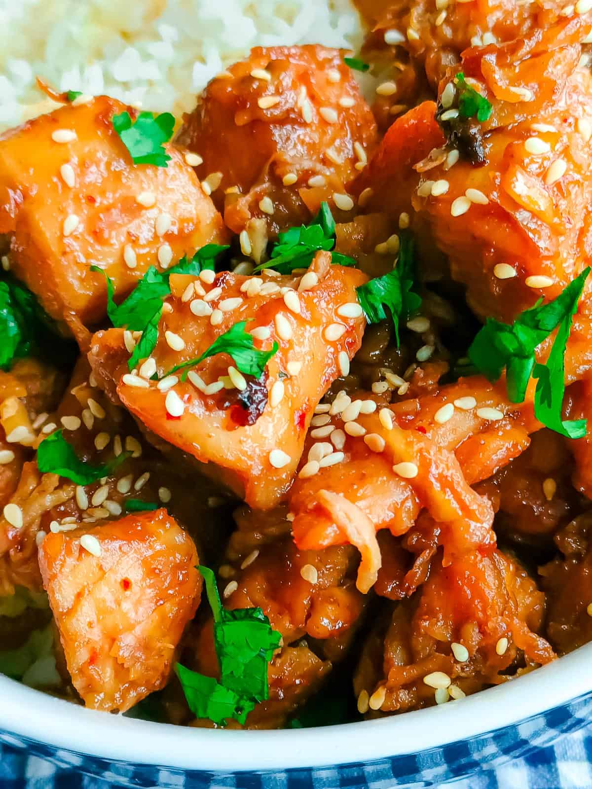 Closeup view of sweet and spicy chicken stir fry with rice in a white bowl.