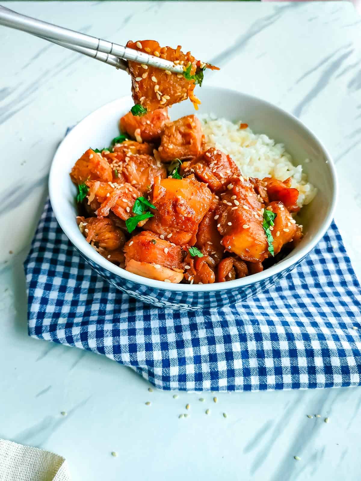 Spicy chicken stir fry with rice in a white bowl with chopsticks.