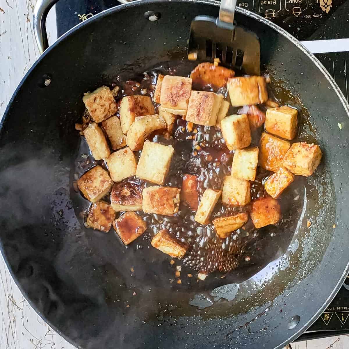 pan fried tofu being added to hot honey garlic sauce.