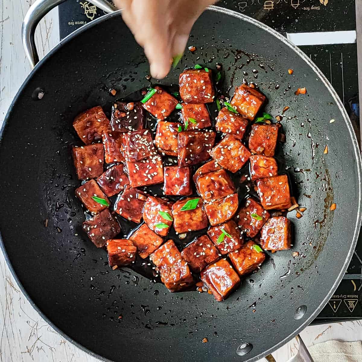 sesame garlic tofu being garnished with sesame seeds.