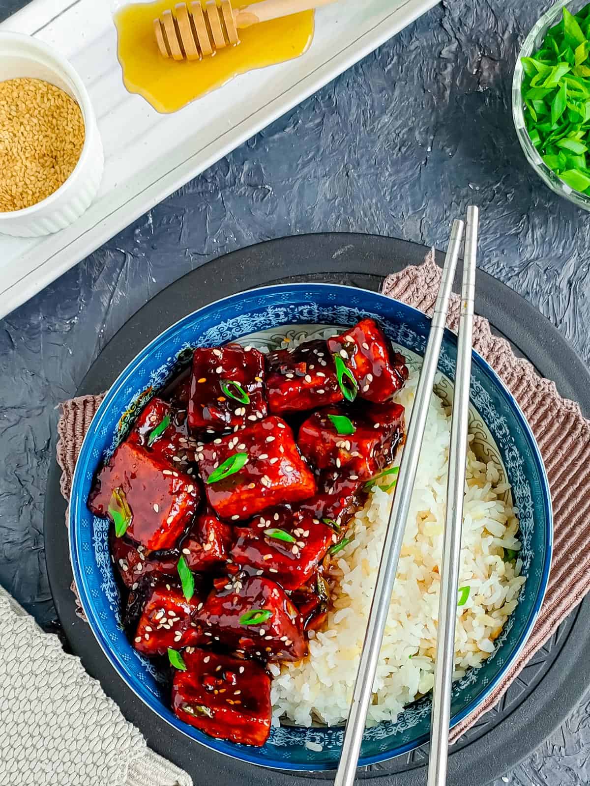 honey soy sticky tofu with rice in a blue bowl with chopsticks.