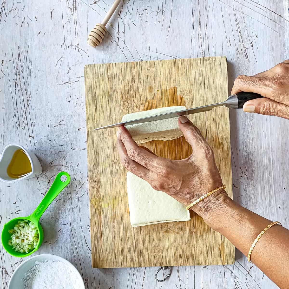 A whole tofu block being sliced horizontally.